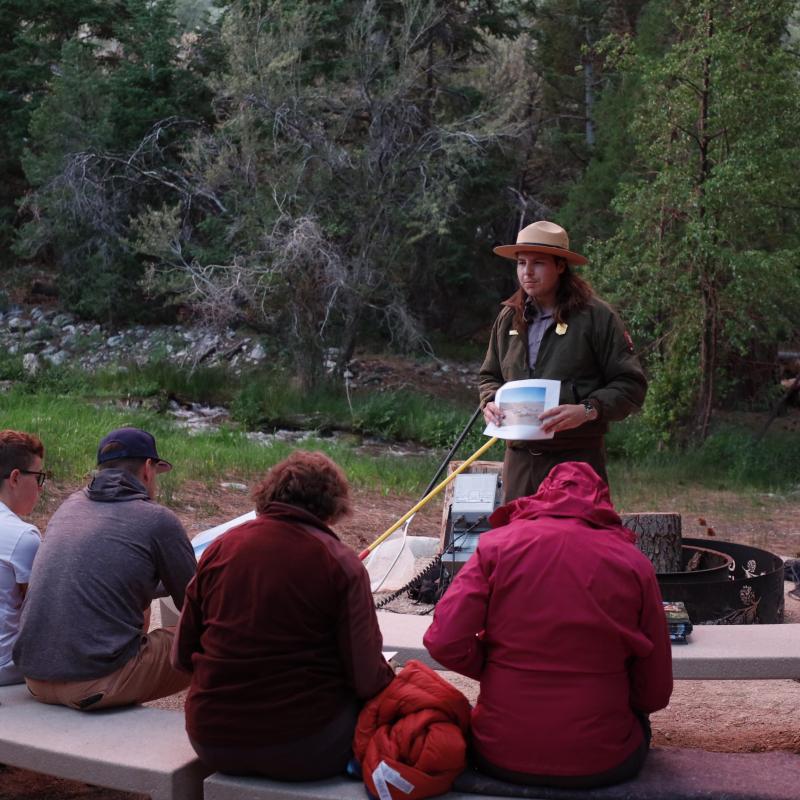 A ranger stands in front of a group of people holding a printed picture in his hands.