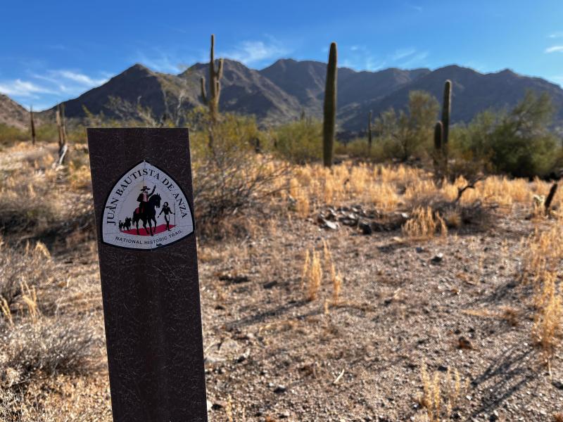 A brown post with an Anza Trail logo marking the trail through a desert landscape