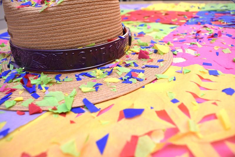 A straw ranger hat with a dark band stamped with “USNPS,” lying on a colorful surface with confetti.