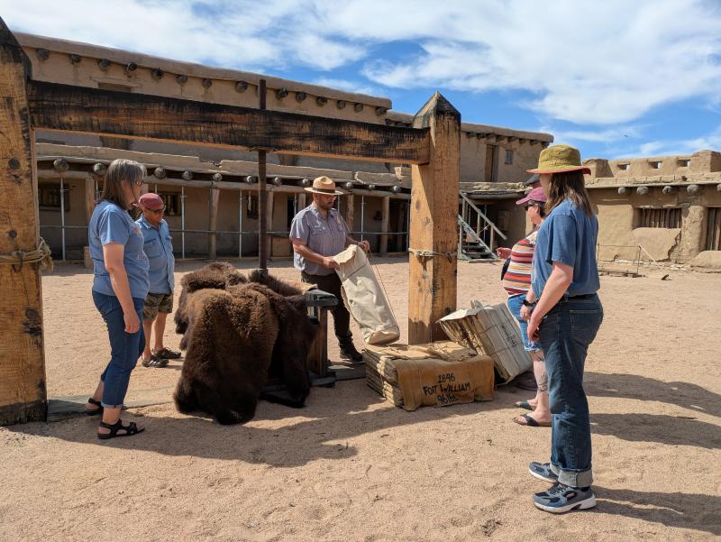 A park ranger and visitors stand near a large wooden fur press