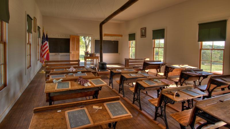 Slate boards and chalk sit on the wooden desks in a single room.