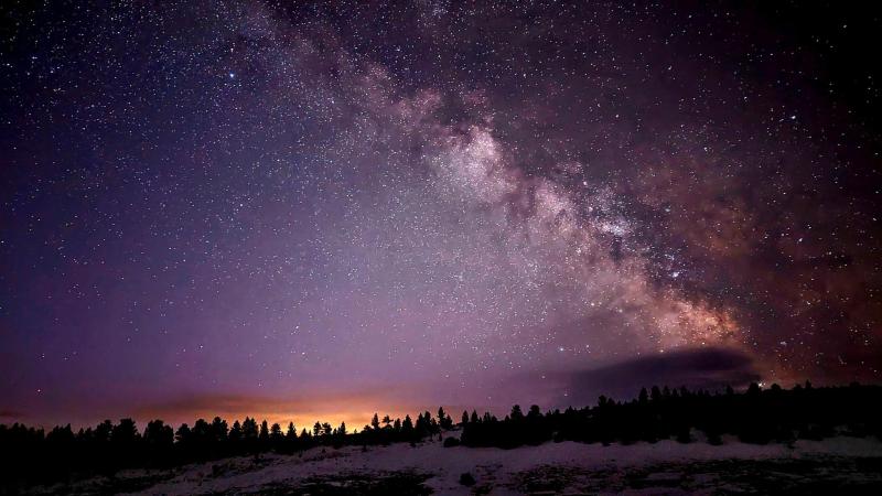 The starry Milky Way Galaxy streaking across a purple and orange night sky.