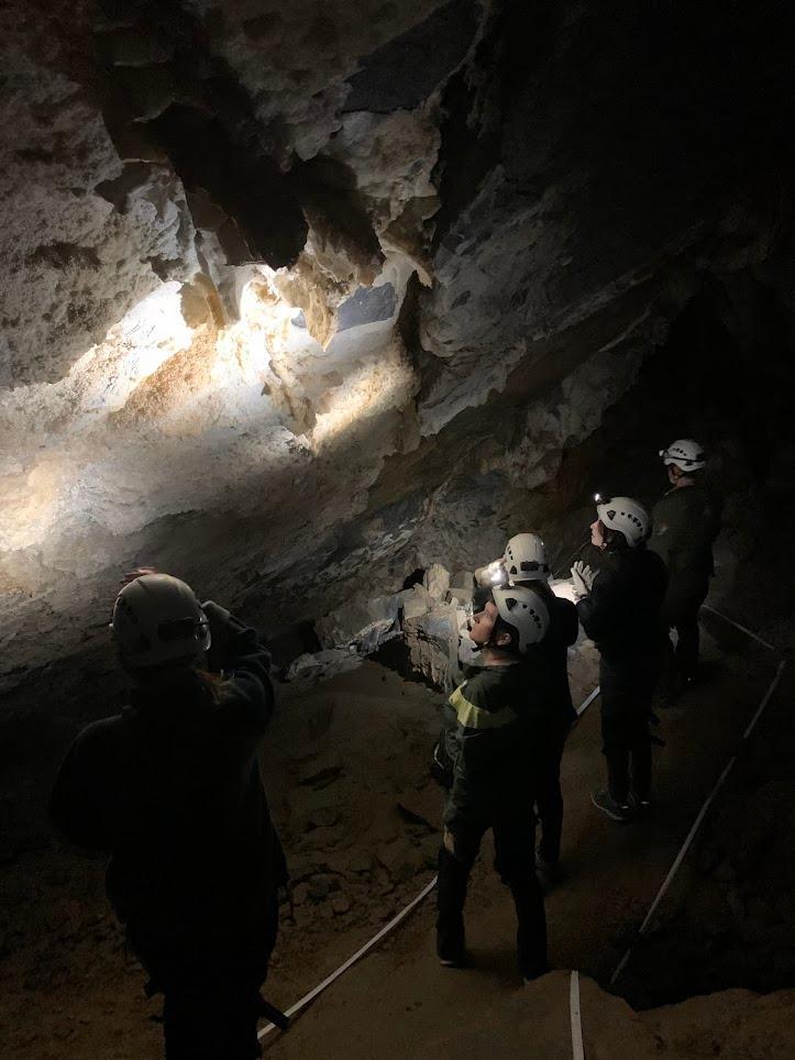 A group of people wearing helmets and headlamps look up at the cave ceiling