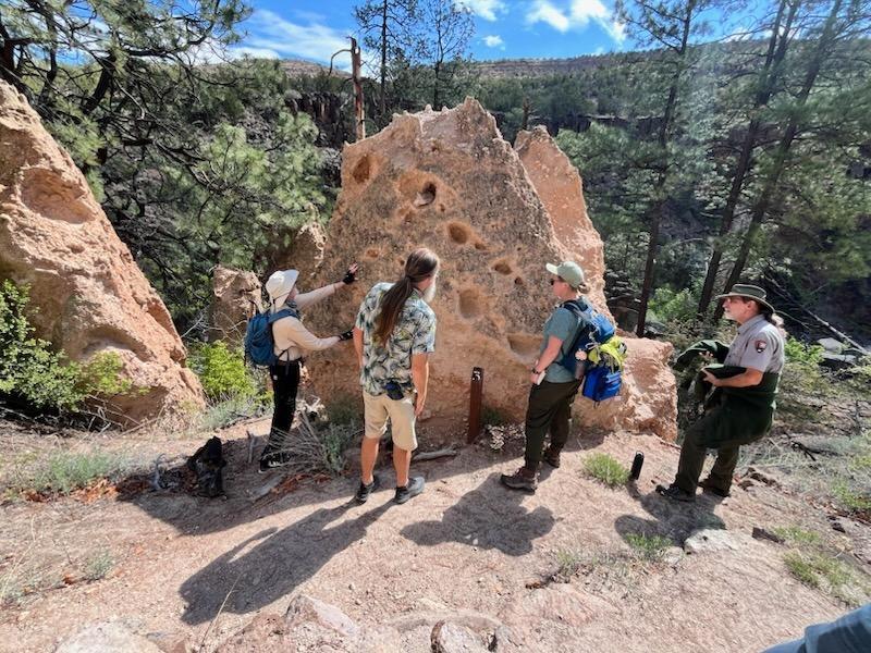 A group of hikers gather around a large holey rock (tent rocks)