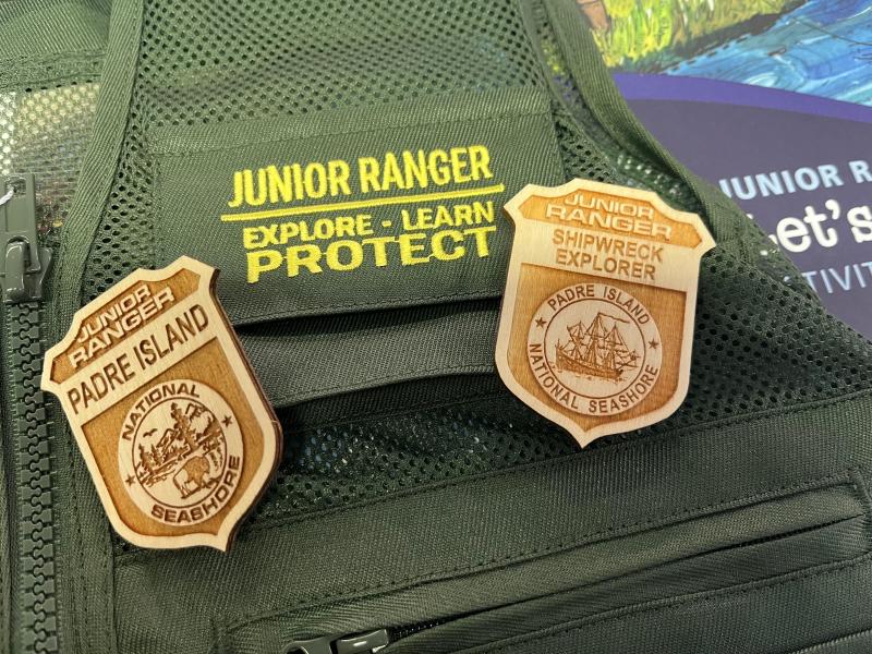 Two junior ranger badges on top of a green junior ranger vest.
