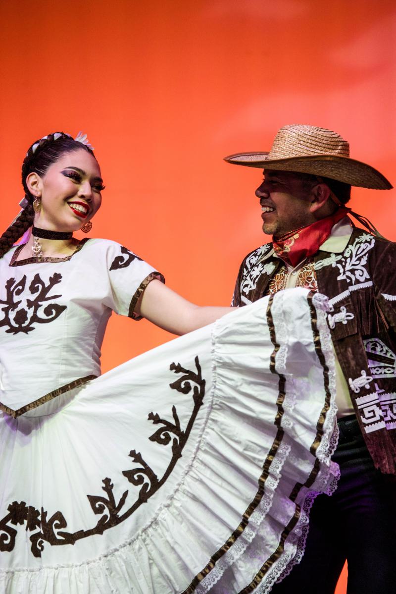 Folklorico dancers face each other on stage.