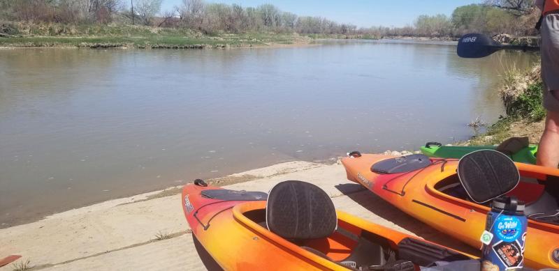 Two orange and red kayaks sit near the waters edge on a boat ramp, ready to be launched.