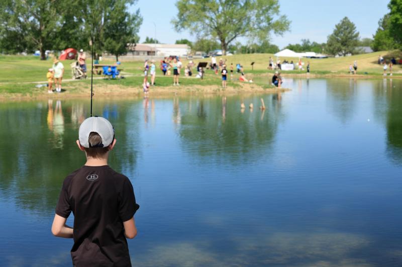 People stand around a still pond fishing