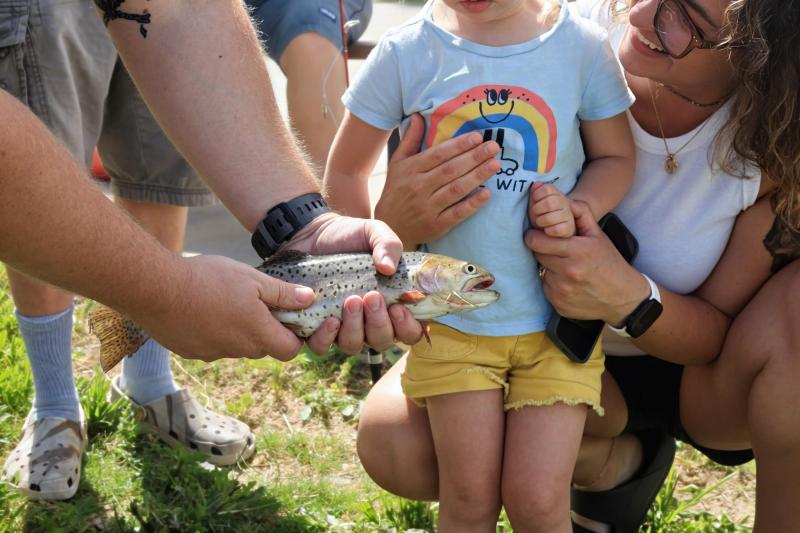 A man holds a fish in front of a young child and a woman.
