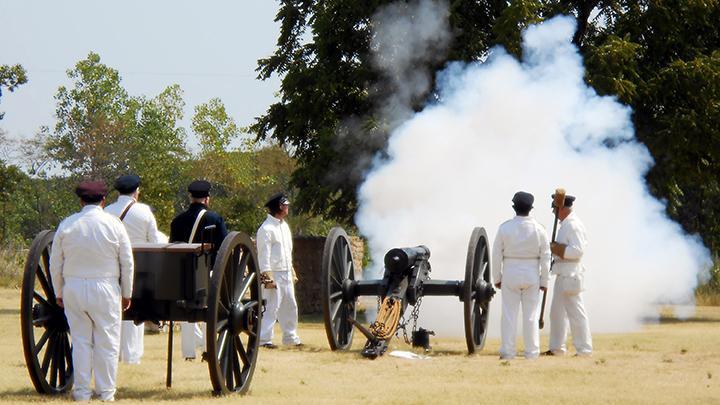 A crew of volunteers dressed in 1840s white uniforms firing a 6lb field cannon.