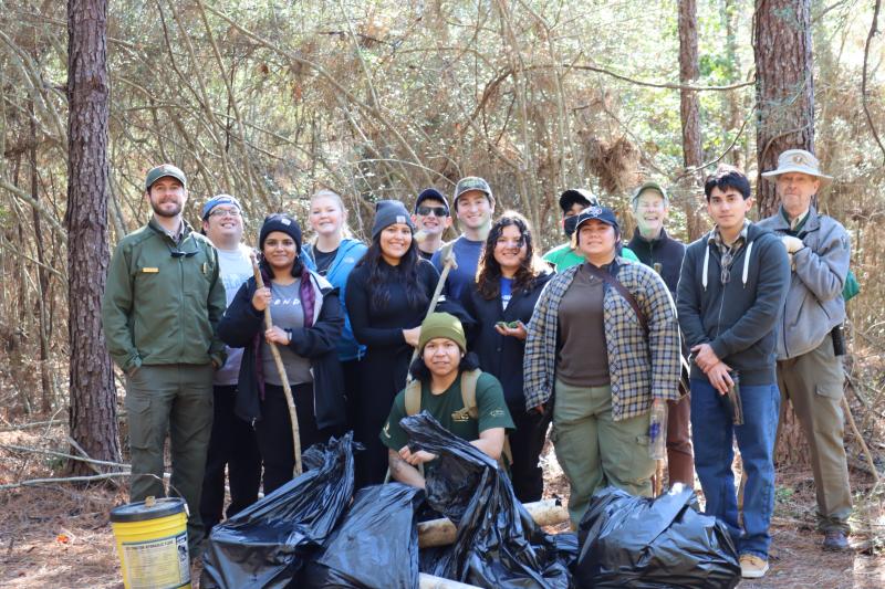 A group of smiling volunteers pose with trash they've collected at one of the Preserve's trails.
