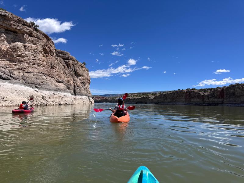 Two orange tandem kayaks paddle along Bighorn Lake near a wall of Bighorn Canyon.