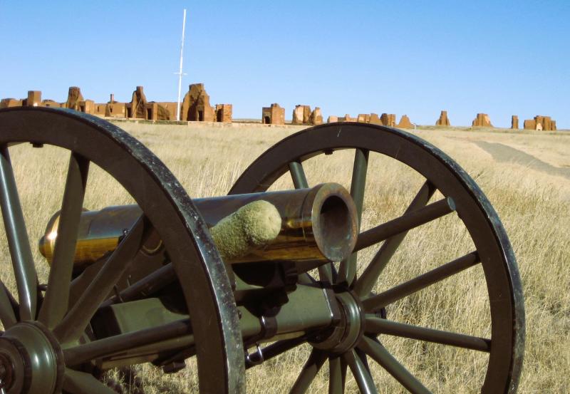 A howitzer and carriage with the adobe ruins of the third Fort Union beyond.