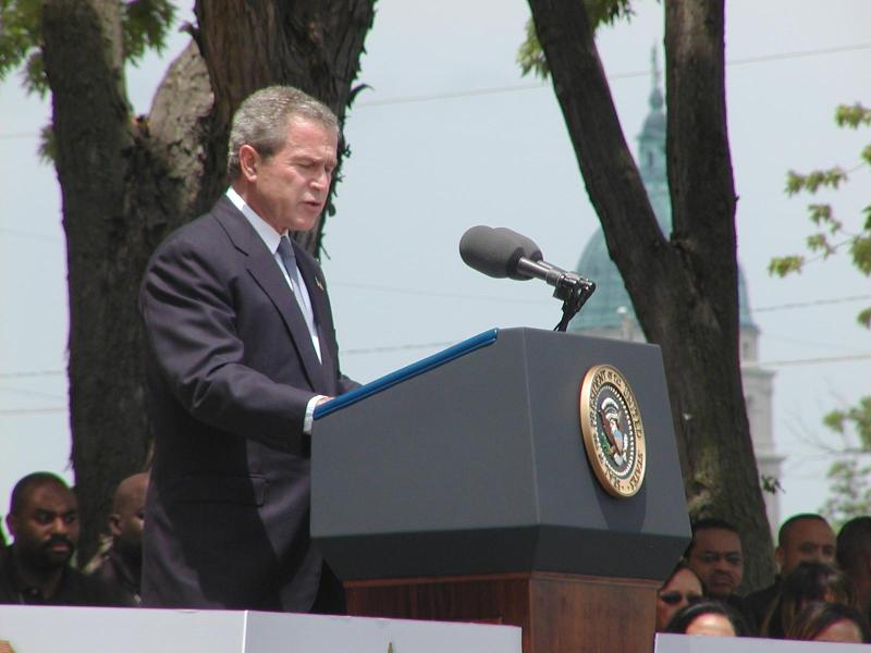 President George W. Bush speaks in front of Monroe School with the Kansas State Capitol behind