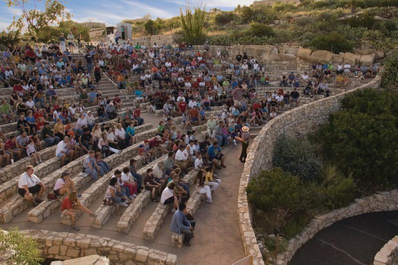 A picture of visitors sitting in a stone amphitheater waiting for the bats to fly out of the cave