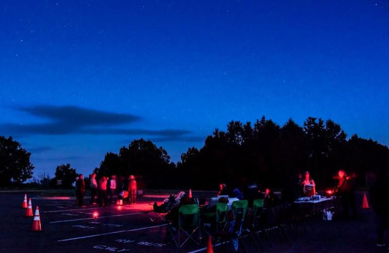 People with telescopes and red light after sunset with trees in the background