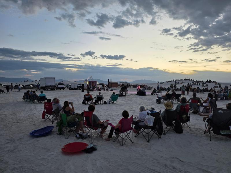 People sitting in chairs on white sand for a concert